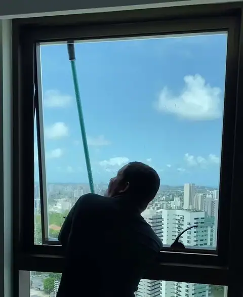 Profissional da Lucas LimpVidros limpando com rodo a janela de um apartamento alto